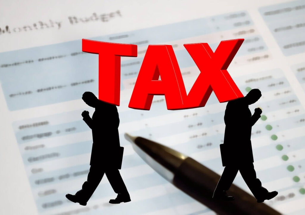 書類の上にボールペンが置かれている写真。その上に"TAX"の文字と、中高年の男性がガッツポーズをしているシャードーイラスト。税対策用の記事目的を表現。